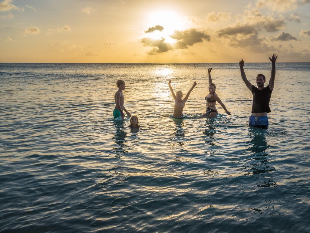 Happy Family with arms in the air in the sea as sun sets on an eco holiday